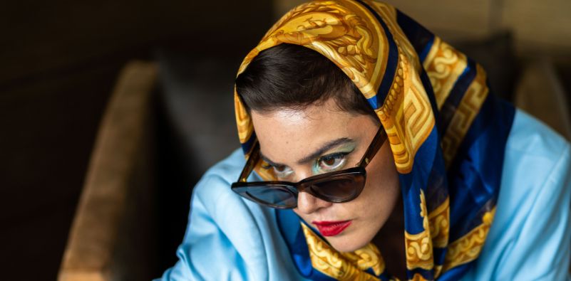A woman wearing a blue and gold silk bandana wearing cat-eye sunglasses