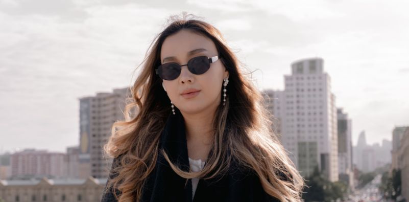 A woman pictured wearing black minimalistic sunglasses with the background of the city