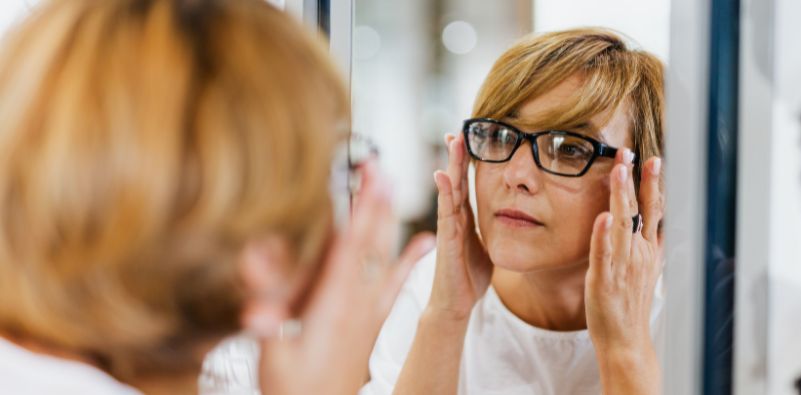 A woman trying on a pair of glasses in the mirror at an opticians.